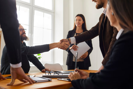 Young business people closing a deal and shaking hands after a successful negotiation meeting in the...