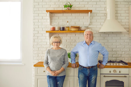 Happy senior couple grandparents standing and looking at camera together in kitchen over interior...