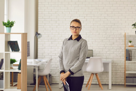Portrait of confident stylish business woman in glasses standing with notebook in hands at modern business center office. Business, confidence and business people concept.の写真素材