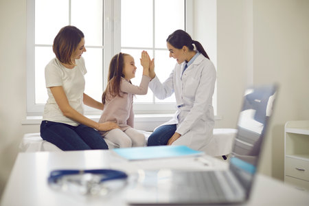 Mum and daughter seeing family practitioner. Happy little girl high-fiving friendly pediatrician during visit to hospital. Healthcare for children, patients positive attitude to doctor, trust conceptの写真素材