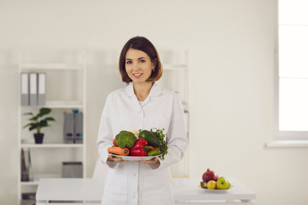 Female nutritionist doctor holds a plate of fresh vegetables in front of her recommending them for diet and weight loss. Concept of a healthy lifestyle and weight loss.の写真素材