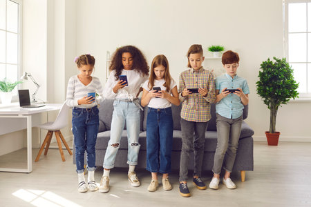 Diverse group of 8-10-year-old children playing online games on smartphones. Kids, immersed in their mobile devices, using learning apps, chatting on social media, blogging and ignoring real lifeの写真素材