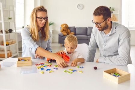 Focused mom, dad and toddler son play and compose words from scattered colored letters. Family sits at home in the living room and spends their free time usefully. Concept of education and developmentの写真素材