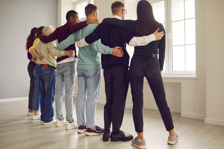 Feeling strong together. Back view of group of mixed-race diverse colleagues or community members standing in row and hugging. Concept of unity and team of people always ready to support each otherの写真素材