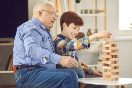 Grandad makes good friend: Happy smiling grandfather and grandson enjoying bonding time and building wooden jenga tower together. Mature man with little child playing fun board game at homeの写真素材