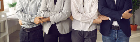 Team of male and female business people standing together in office, holding hands, supporting each...