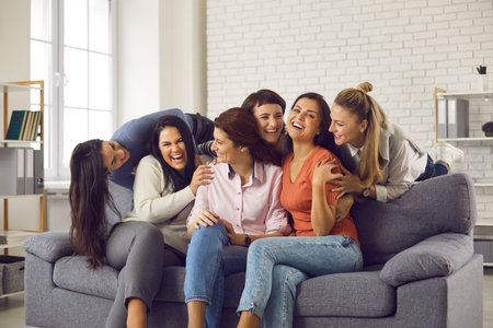 Group of happy friends having fun and enjoying free time together. Carefree young women sitting on sofa at home, laughing and fooling around. Concept of friendship, sharing happiness, mutual supportの写真素材