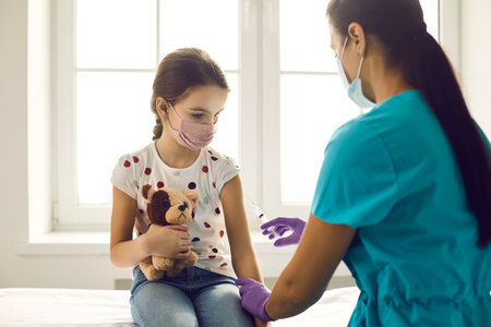 Young nurse or doctor is about to gently inject a vaccine into the hand of a cute little girl...