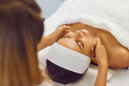 Cosmetologist making facial massage treatment for serene young woman with hands in beauty spa salon, top view, close-up. Facial treatment, massage, skincare, cosmetology conceptの写真素材