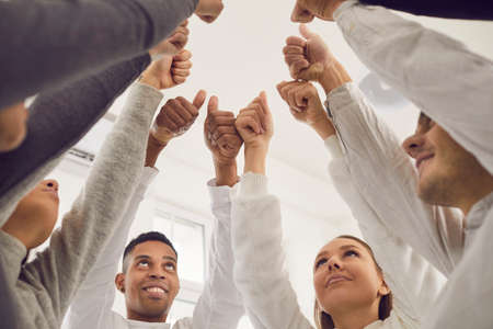 Business concept. Team of happy friends celebrating teamwork and success in group meeting. Low angle of young people joining hands and giving thumbs-up, all together voting for good idea or suggestionの写真素材