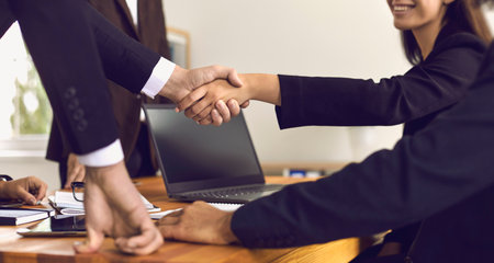 Closeup of people shaking hands above office desk making successful business deal. Happy company...