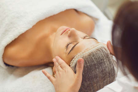 Face massage. Close-up of young woman getting spa massage treatment at beauty spa salon. Masseur makes acupressure on a female face. Spa skin and body care. Facial beauty treatment.の写真素材