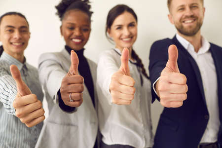 Group of happy smiling confident young multiracial business men and women giving thumbs-up together, closeup. Excellent choice, good result, success, winning solution, office job satisfaction conceptの写真素材