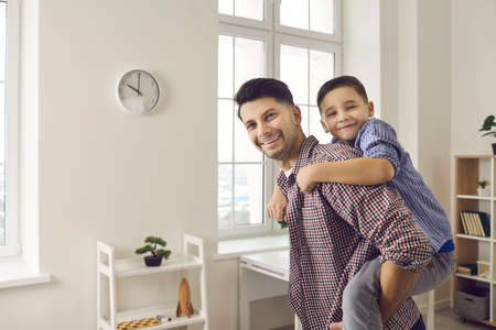 Happy family. Portrait of a loving father playing with his son at home carrying him on his back. Fathers day.Dad and his kid having good time together. Concept of family, fatherhood and childhood.の写真素材