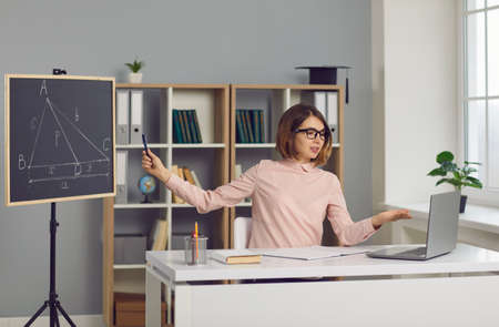 School math teacher sitting at laptop computer and giving engaging virtual lesson. Young woman in...
