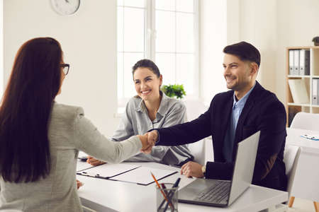 Happy smiling married couple making a handshake with a lawyer, realtor or financial advisor. Man and...