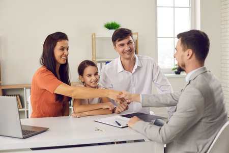 Happy family with child meeting with manager at real estate agency. Smiling husband and wife shaking hands with agent and thanking him for help. Buying new house and signing purchase agreement conceptの写真素材