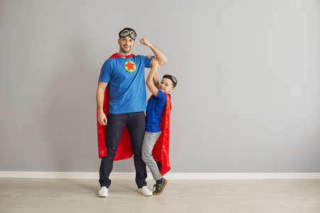 Portrait of family with super powers. Happy young dad and little child dressed as superheroes playing and having fun together. Father and son in hero capes standing in studio and looking at cameraの写真素材