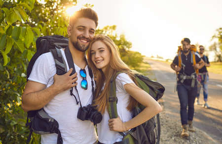 Young couple of tourists with backpacks with friends on a trip in nature. Hikers are walking in the countryside.の写真素材