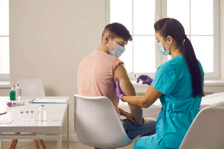 Vaccination against during epidemic concept. Young man patient in protective face mask sitting and...