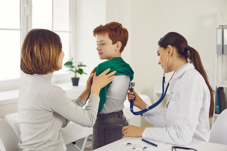 Woman doctor pediatrician in medical uniform examining little smiling boy with stethoscope with caring mother sitting near during checkup and consultation in medical clinic office. Medicare for kidsの写真素材