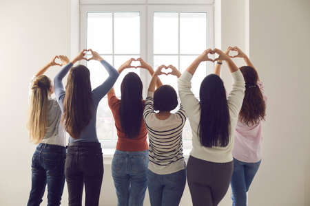 Team of women standing together by window and doing heart shaped sign hand gesture. Group of six young ladies willing to make world better place. Love, harmony, gratitude, support, solidarity conceptの写真素材