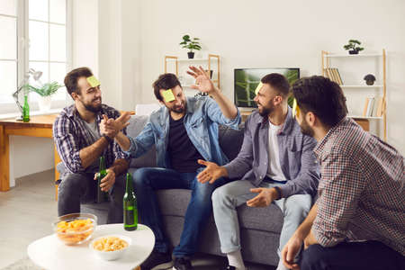 Happy people having fun at home. Young men enjoying weekend together. Group of adult friends sitting...
