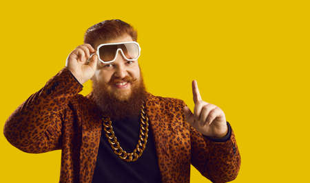 Rich, chubby, plus size, bearded young man with handlebar mustache in party outfit, gold neck chain, and cool glasses looking at camera and pointing finger up. Good idea and number one rule conceptの写真素材