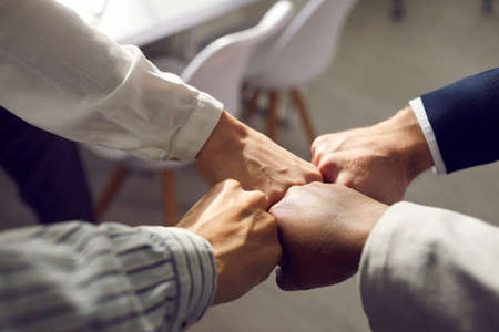 Close up of hands of business partners folding fists together as a symbol of unity. Four people bumping their fists together in an office at a meeting. Concept of trust, friendship and cooperation.の写真素材