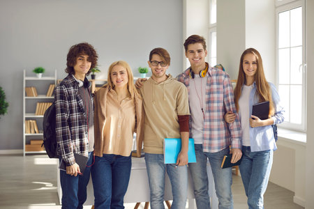 Group of happy young people in casual wear standing in modern classroom at uni. Portrait of five smart high school, college or university students smiling and looking at camera all togetherの写真素材