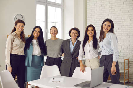 Group portrait of happy successful beautiful business women. Team of positive cheerful young female professionals in their 20s and 30s standing close together in company office and smiling at cameraの写真素材