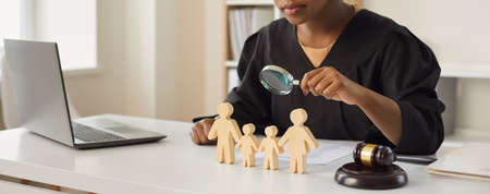 African american judge looking through magnifying glass at wood family figure making decision on...