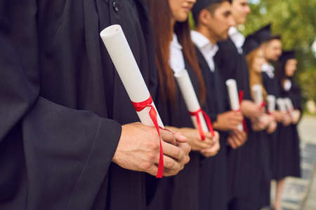 Close-up of young university graduates hands holding diplomas after university graduating outdoors, selective focus. Graduating from university or college conceptの写真素材