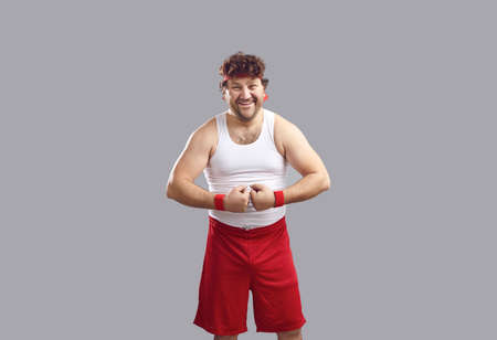 Happy man with curly hair in headband, white tank top and red shorts smiling and flexing arms...
