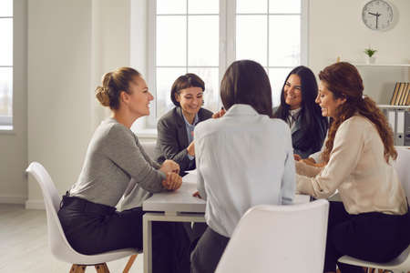 Team of women planning new project and choosing business strategy together. Group of positive businesswomen in their 20s and 30s meeting around office table, sharing opinions and discussing ideasの写真素材
