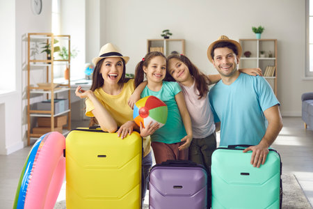 Weve packed suitcases and are ready for holiday. Happy young parents and little kids having fun at home before summer vacation trip. Portrait of smiling family with colorful cases looking at cameraの写真素材
