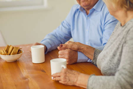 Close up in the morning senior couple holding hands sitting at the table and drinking tea. Mature man and woman start the day correctly and positively. Concept of family, love, support and intimacy.の写真素材