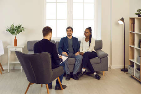 Pleased happy mixed race couple meeting family psychiatrist or financial advisor. Male counselor...