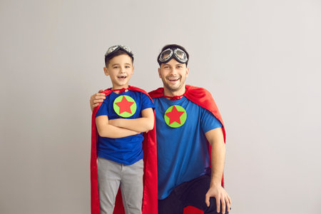 Happy laughing father and cheerful preschool son dressed superhero red cloak and mask posing for camera. Studio shot family parent and child portrait. Parenthood, fatherhood and childhoodの写真素材