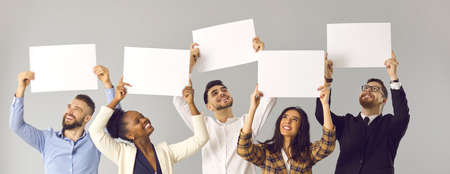 Banner with group of five happy smiling diverse people, colleagues or friends, expressing opinion and giving positive feedback holding white mockup signs and sheets of paper on gray studio backgroundの写真素材