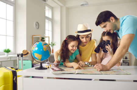 Family vacation planning, worldwide travelling, booking flight ticket. Happy mother and father with daughter children searching tourist route on paper map, choosing country to travel, tropical resortの写真素材