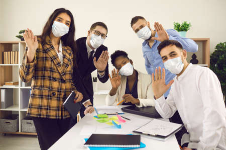 Portrait of happy creative office worker colleague team wearing protective face mask to prevent Covid-19 spreading waving hello hand gesture looking at camera smiling. Business lifestyle new normalの写真素材