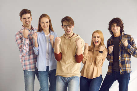 Group of happy excited cheerful young people in casual wear fist pumping and having fun celebrating achieving goal, sports team victory, business success, getting scholarship, winning education grantの写真素材