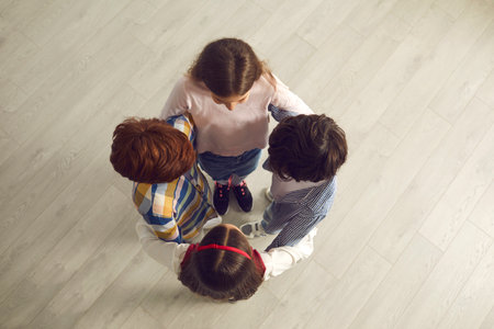 View from above of group of children. Four little kids standing close in circle and holding hands. Social communication, interaction, help, cooperation, connection, improving peer relationship conceptの写真素材