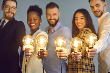 Happy creative team holding glowing lit lightbulbs. Diverse collaboration group of intelligent young multicultural business people with shining light bulbs presenting and sharing effective useful ideaの写真素材