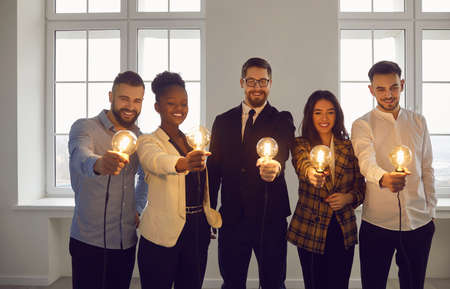 Happy enthusiastic multiracial business team with shining light bulbs. Group of smiling inspired...