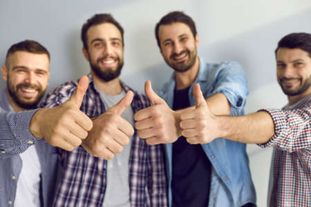 Fiendship and approval. Male friends show pleasure and give a positive feedback showing thumbs up against the gray wall. Close up of thumbs up of young men showing cool gesture. Selective focus.の写真素材