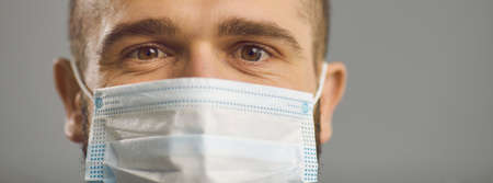 Closeup studio portrait of caucasian man in face surgical mask looking at camera over gray background. healthcare, airborne respiratory illness, air pollution protection awarenessの写真素材
