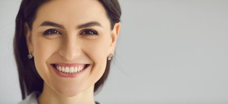 Close up of the face of a woman who is sincerely smiling with a snow-white smile on a gray...