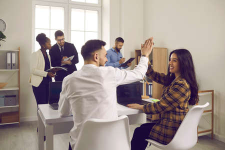 Well done. Happy enthusiastic people high-five each other sitting at table in coworking office....